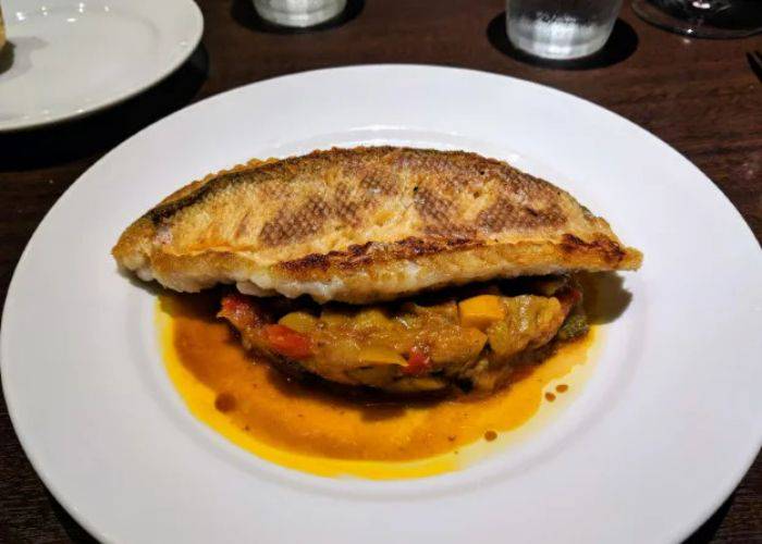 Crispy fish is laid on top of a bed of fresh vegetables, surrounded by a sauce.